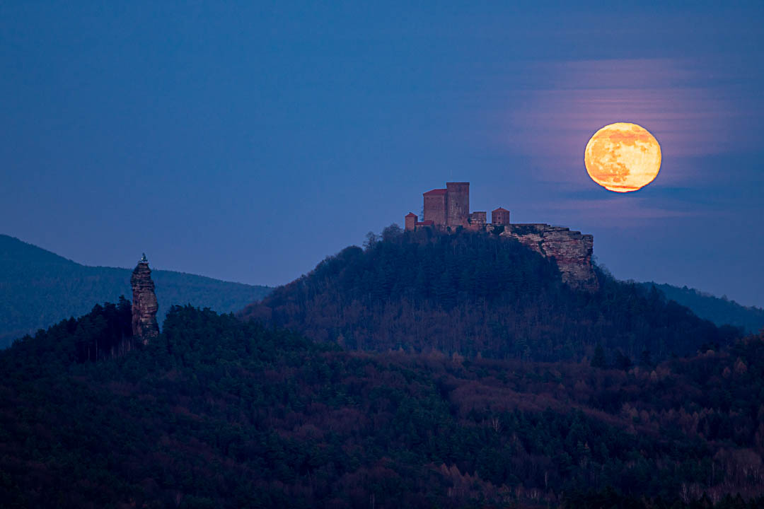 Vollmond über der Burg Trifels. Roter Vollmond verzerrt durch die Luftbewegungen zarte Wolkenschlieren, rechts noch der Kletterfelsen Asselstein