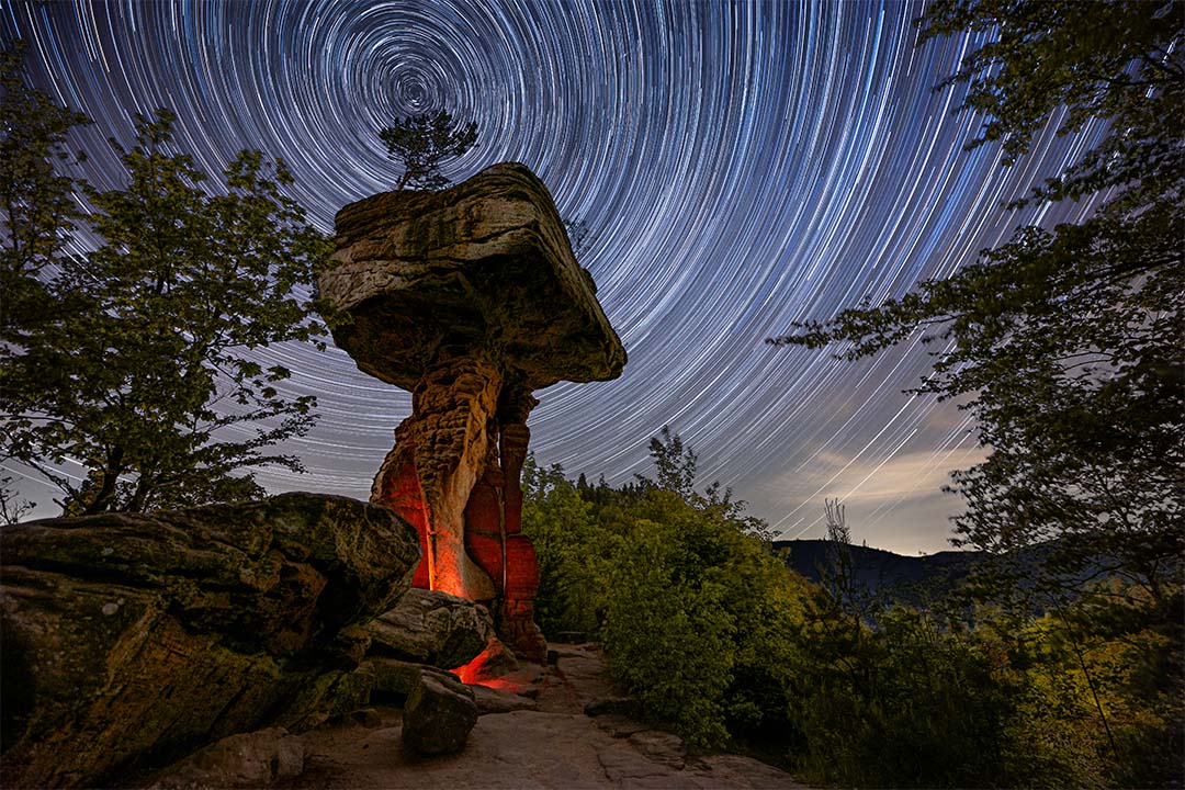 Startrail bzw. Sternenspuren überm Teufelstisch. Nächtliche Aufnahme des bekannten Sandsteinfelsens mit rötlicher Beleuchtung