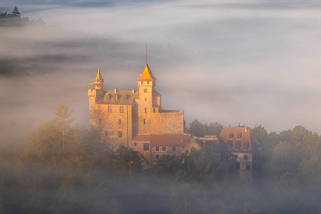 Herbst an der Burg Berwartstein. Fette Nebelschwarten umgarnen die Burg und die Sonne beleuchtet den Turm
