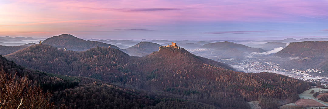 Wintermorgen über Annweiler und den Burgen Trifels, Anebos und Münz. Die Lärchen schimmern gelb, die Sonne beleuchtet schon die Burgen und die Gegendämmerung ist auf ihrem Höhepunkt