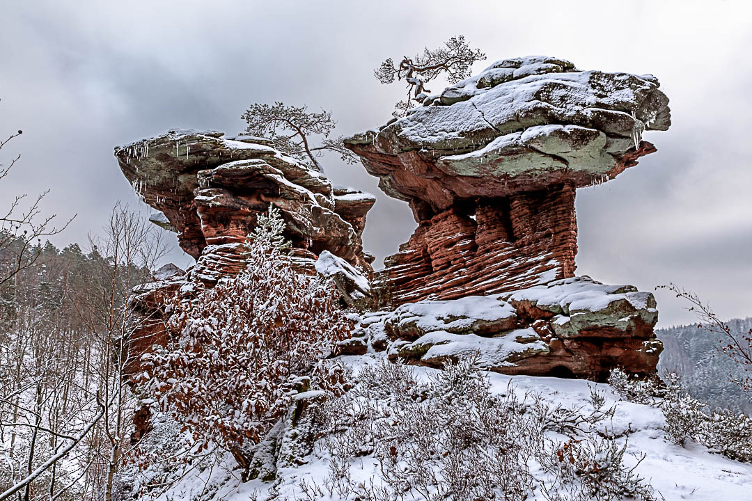 Wolkenverhangender Winterabend am Sattelfels, der voller Schnee ist und Eiszapfen von dem Sandsteinfelsen herabhängen.