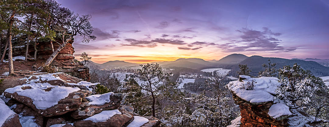 Winterlicher Morgen mit einem schneebecketen Pfälzerwald und einem farbenprächtigen Himmel am Sprinzelfelsen